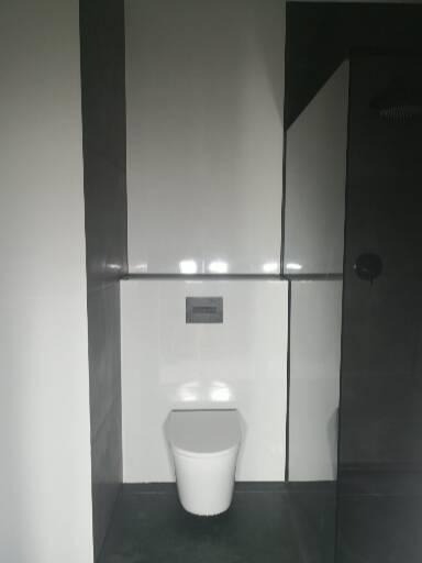 Nowoczesna łazienka z białym sedesem podtynkowym, białe płytki na ścianach z szarymi akcentami, ciemna podłoga.