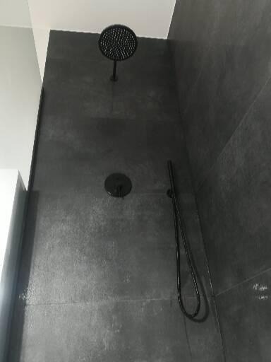 Czarna deszczownica i bateria podtynkowa zamontowane na ścianie z szarych, matowych płytek w nowoczesnej łazience.