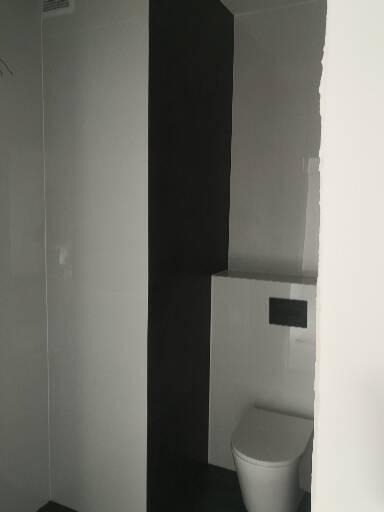 Nowoczesna toaleta podwieszana w wykończonej łazience w Elblągu, z czarnym pasem na ścianie i białymi płytkami.