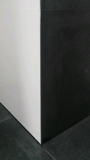 Styk białej ściany z czarną, wykończonej czarnymi płytkami podłogowymi z wyraźnymi fugami.