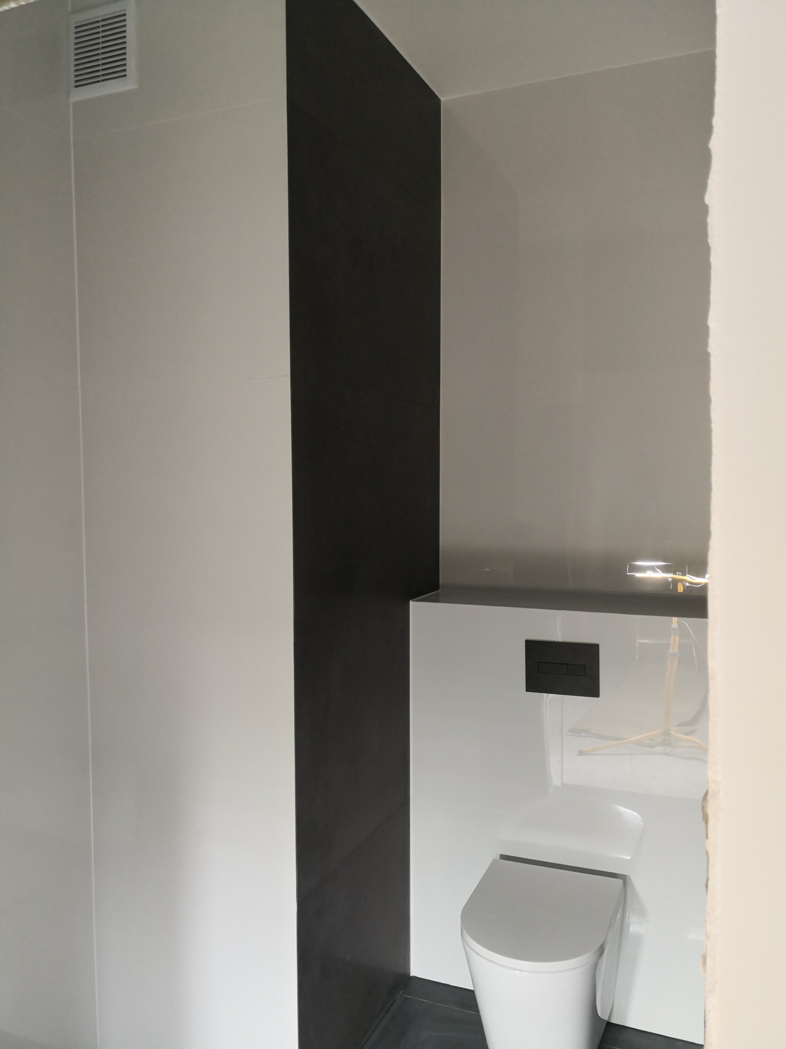 Nowoczesna łazienka z białą ceramiką, czarną płytką akcentującą i minimalistycznym systemem spłukiwania podtynkowego.