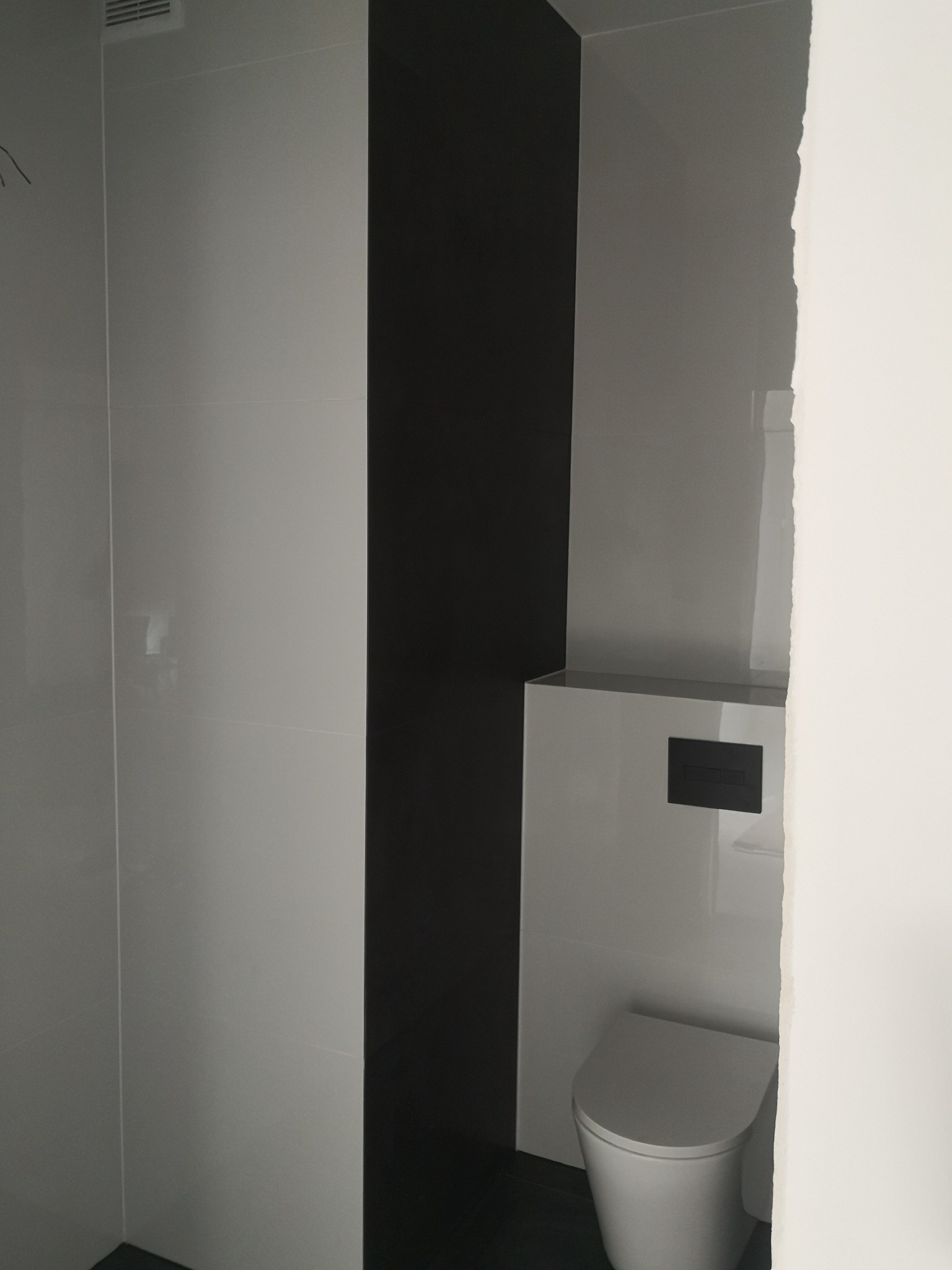 Nowoczesna łazienka z białymi płytkami, czarnym pasem płytek i podwieszaną toaletą z czarnym panelem sterującym.