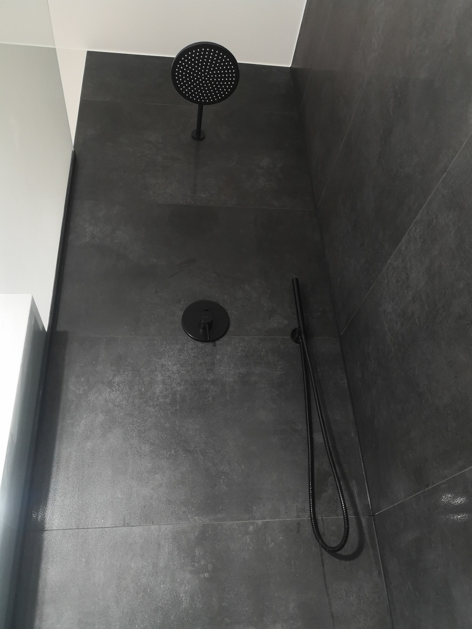 Nowoczesna kabina prysznicowa z czarną armaturą i szarymi płytkami imitującymi kamień, widok z dołu.