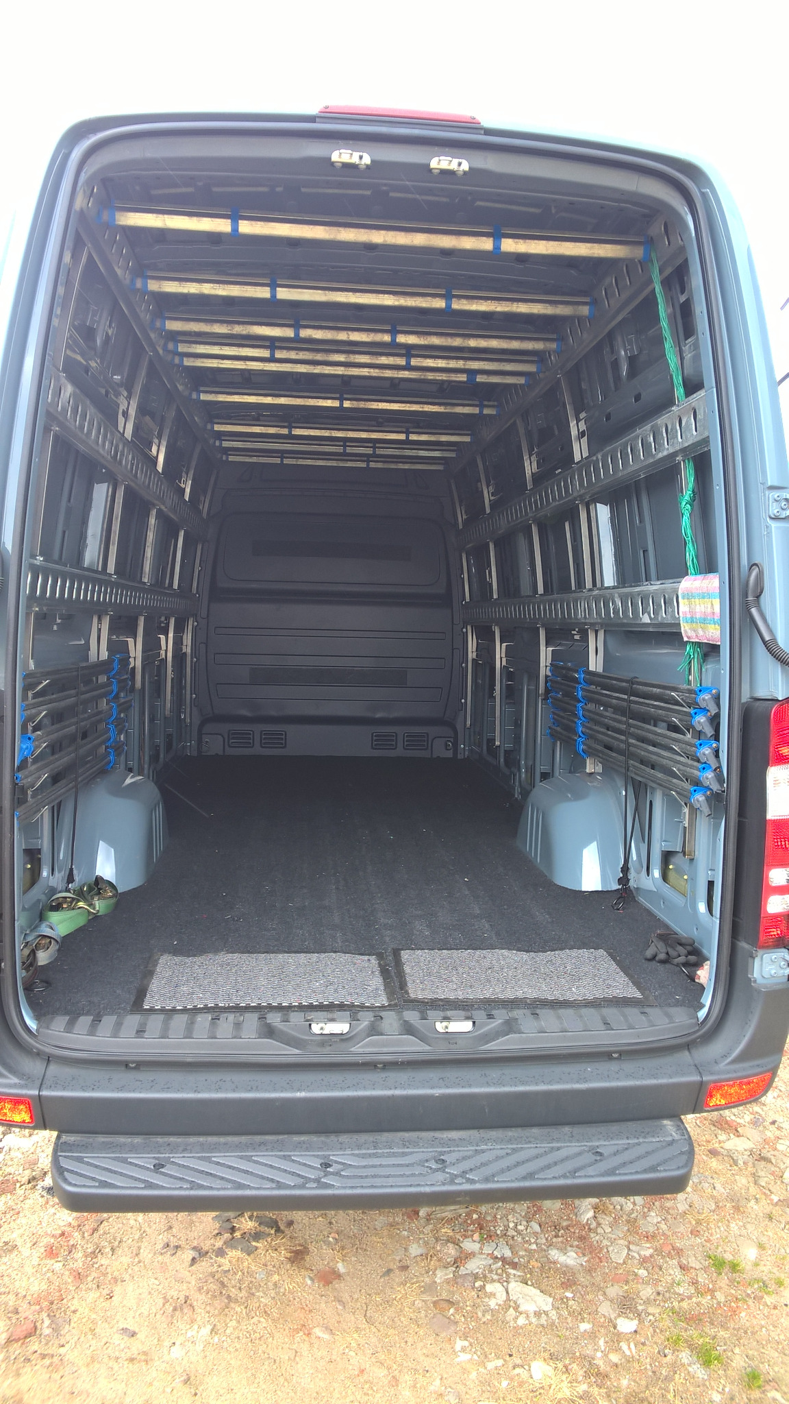 Wnętrze dostawczego samochodu z zamontowanym systemem poprzeczek i uchwytów do przewozu odzieży wiszącej, widok z tyłu pojazdu.