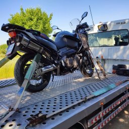 AUTO-JACK Jacek Mróz - Czarny motocykl zabezpieczony pasami na platformie lawety, widok z boku z elementami otoczenia.