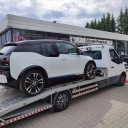 AUTO-JACK Jacek Mróz - Białe BMW i3 na lawecie przed salonem samochodowym Zdunek Premium, widoczne tablice rejestracyjne i elementy zabezpieczające auto.
