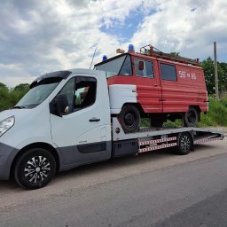 AUTO-JACK Jacek Mróz - Biała laweta przewozi czerwono-biały wóz strażacki z numerem 597-66 na tle pochmurnego nieba i zieleni.
