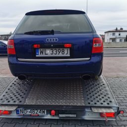 AUTO-JACK Jacek Mróz - Niebieskie Audi kombi na lawecie w Warszawie, widok z tyłu, tablice rejestracyjne WL 3398J i NO 4824W, w tle budynki i droga.