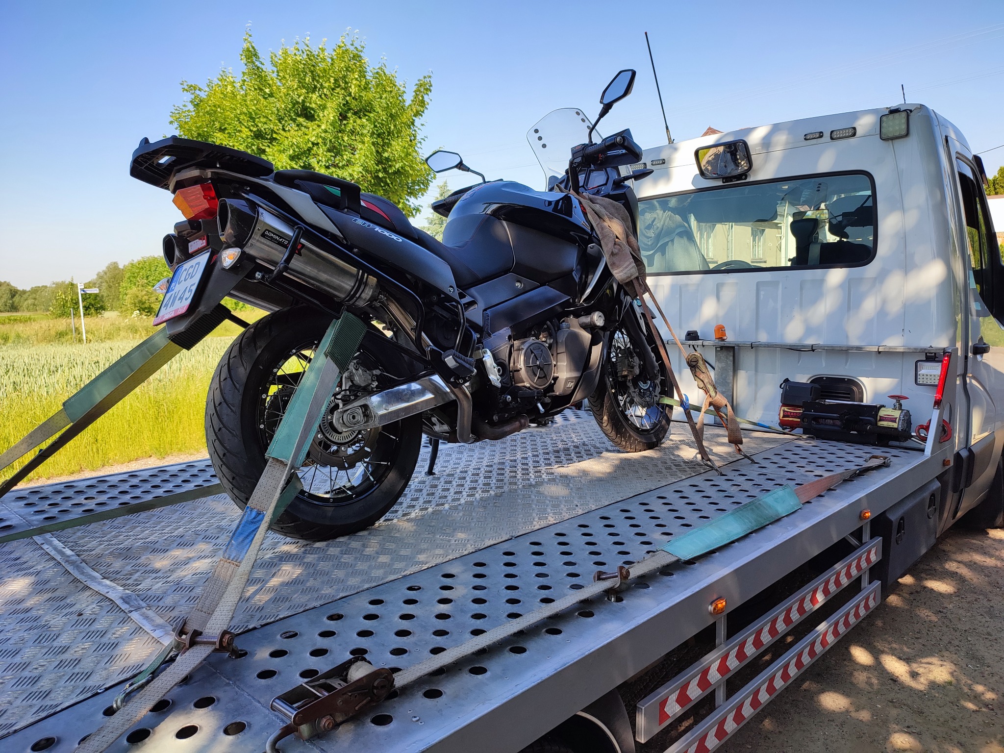 Czarny motocykl zabezpieczony pasami na platformie lawety, widok z boku z elementami otoczenia.