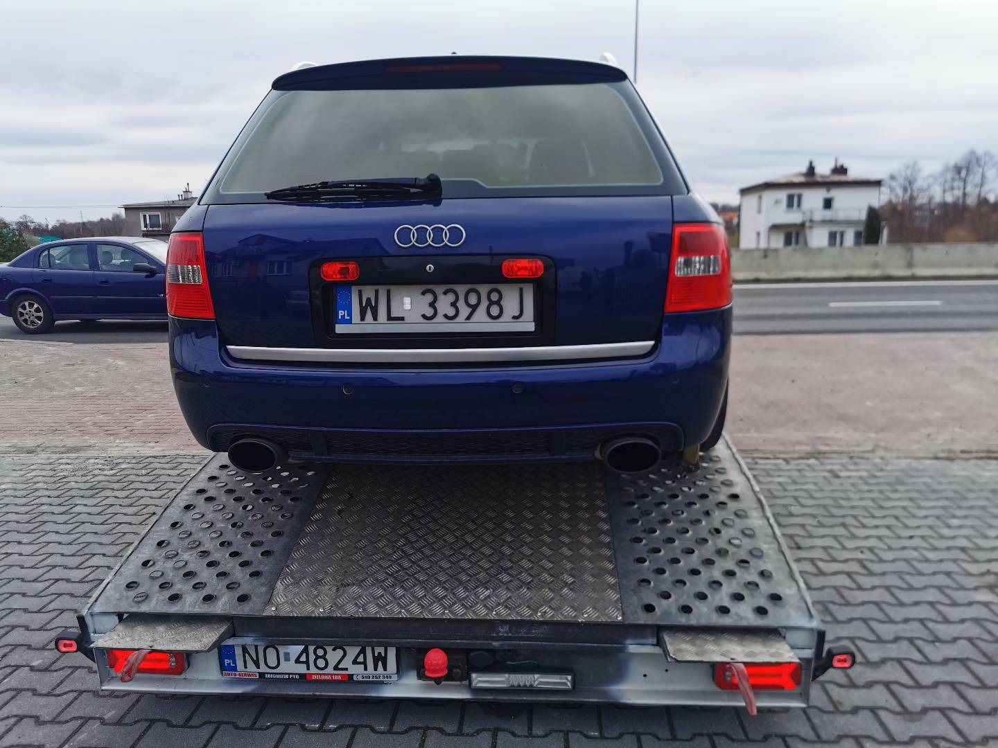 Niebieskie Audi kombi na lawecie w Warszawie, widok z tyłu, tablice rejestracyjne WL 3398J i NO 4824W, w tle budynki i droga.