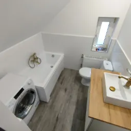Nowoczesna łazienka na poddaszu z białymi płytkami, drewnopodobną podłogą, umywalką z baterią w stylu retro, białą wanną, toaletą i pralką.