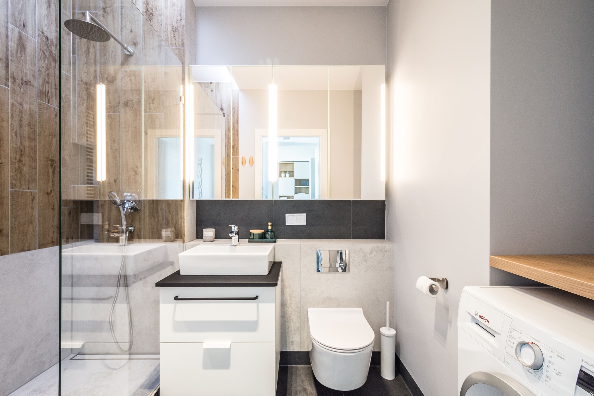 Nowoczesna łazienka z prysznicem typu walk-in, umywalką nablatową na szafce, podświetlanym lustrem, toaletą i pralką Bosch.
