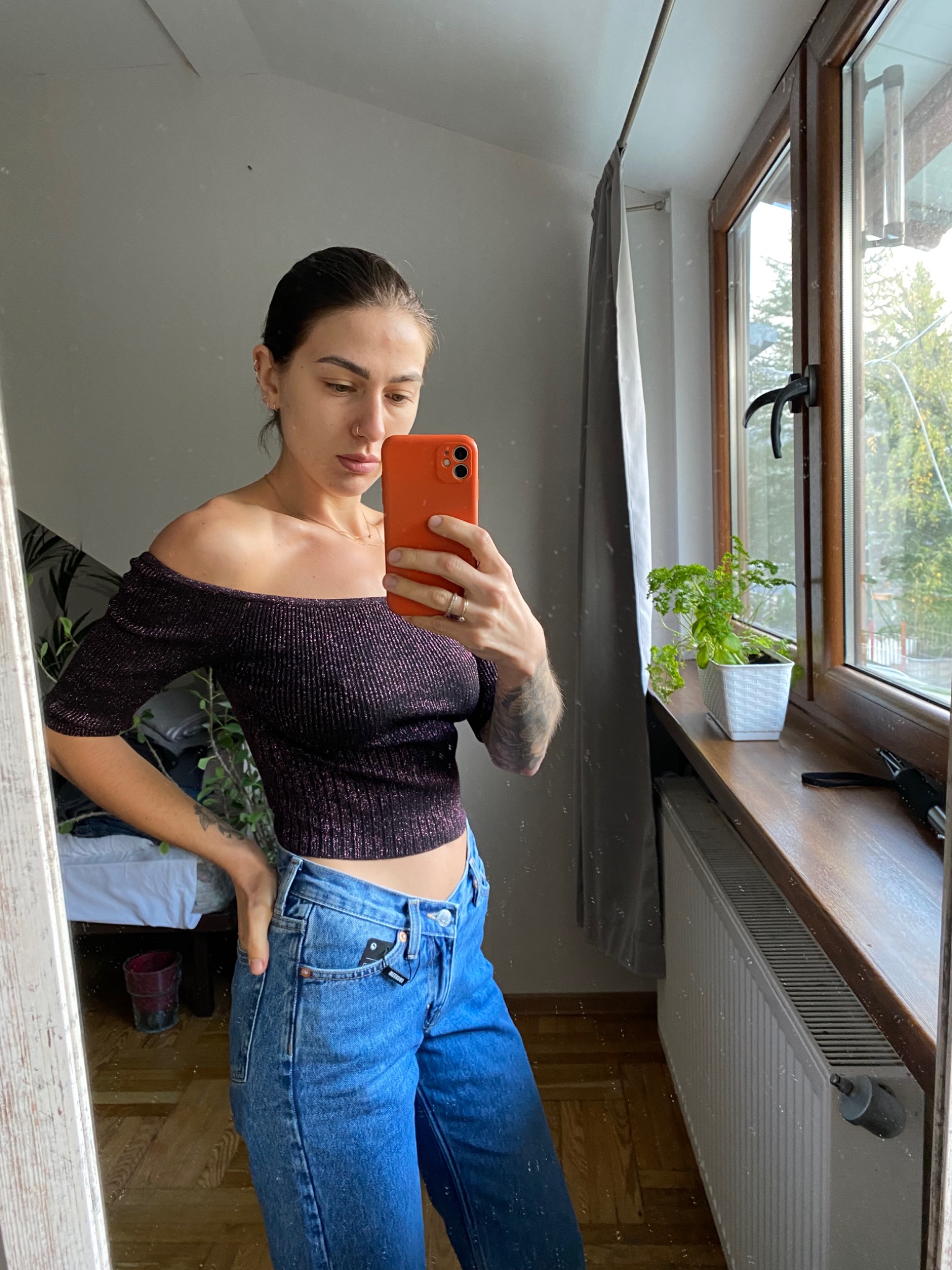 Kobieta robi selfie w lustrze, ubrana w bluzkę z odkrytymi ramionami i dżinsy. W tle widoczne okno z widokiem na Karpacz.