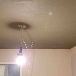 Miczada - Niedokończony sufit z nałożoną warstwą gładzi, widoczne ślady po szpachlowaniu, wisząca żarówka na kablu, fragment ściany z resztkami starej farby.