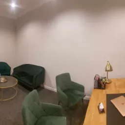 Wnętrze biura w Lublinie z zielonymi fotelami, drewnianym biurkiem z laptopem i złotą lampką, oraz rośliną doniczkową na parapecie.