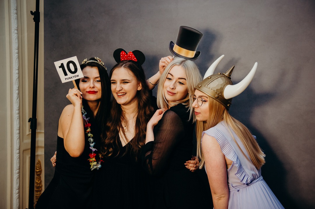 Cztery uśmiechnięte kobiety pozują do zdjęcia w przebraniach: korona, uszy Myszki Miki, cylinder i hełm wikinga z rogami, trzymając tabliczkę z napisem '10 punktów'.