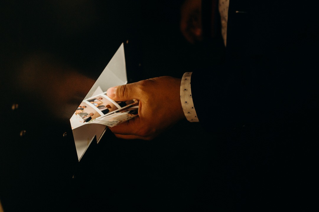 Mężczyzna w garniturze wyjmuje paski ze zdjęciami z fotobudki, widoczny mankiet koszuli w kropki.