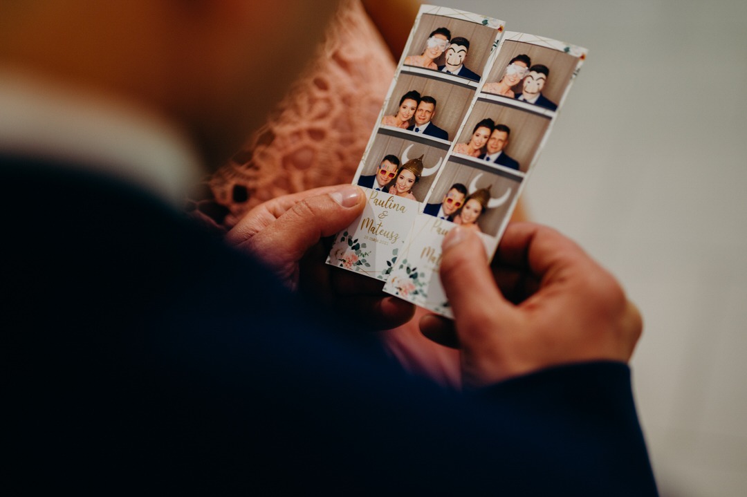 Mężczyzna trzyma w dłoniach paski zdjęć z fotobudki, na których widać parę w przebraniach i z datą ślubu.