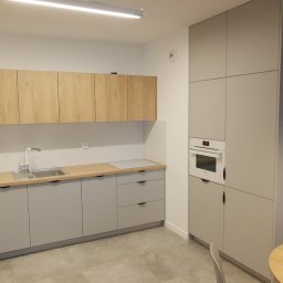 Daniel Woźniak-Matuszewski - Nowoczesna kuchnia z szarymi szafkami dolnymi i górnymi z drewnianym wykończeniem, zintegrowanym piekarnikiem i blatem z jasnego drewna.