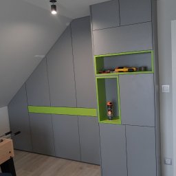 Daniel Woźniak-Matuszewski - Szara zabudowa meblowa pod skosem z zielonymi akcentami, wnęki z zabawkami i sprayem, widoczny fragment piłkarzyków.