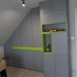 Szara zabudowa meblowa pod skosem z zielonymi akcentami, wnęki z zabawkami i sprayem, widoczny fragment piłkarzyk&oacute;w.