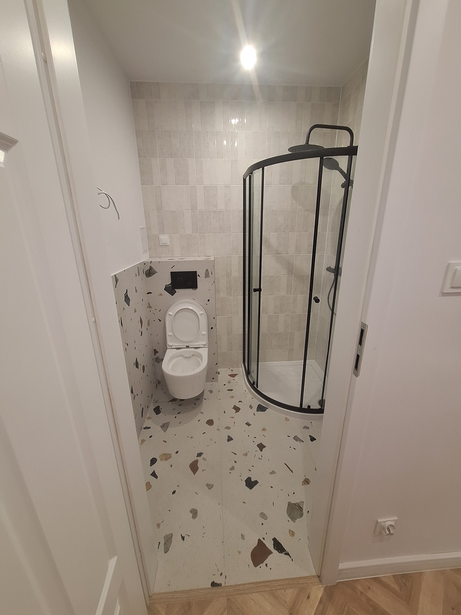 Nowoczesna łazienka po remoncie z kabiną prysznicową z czarnymi profilami, wiszącą toaletą i płytkami lastryko na podłodze i obudowie stelaża.