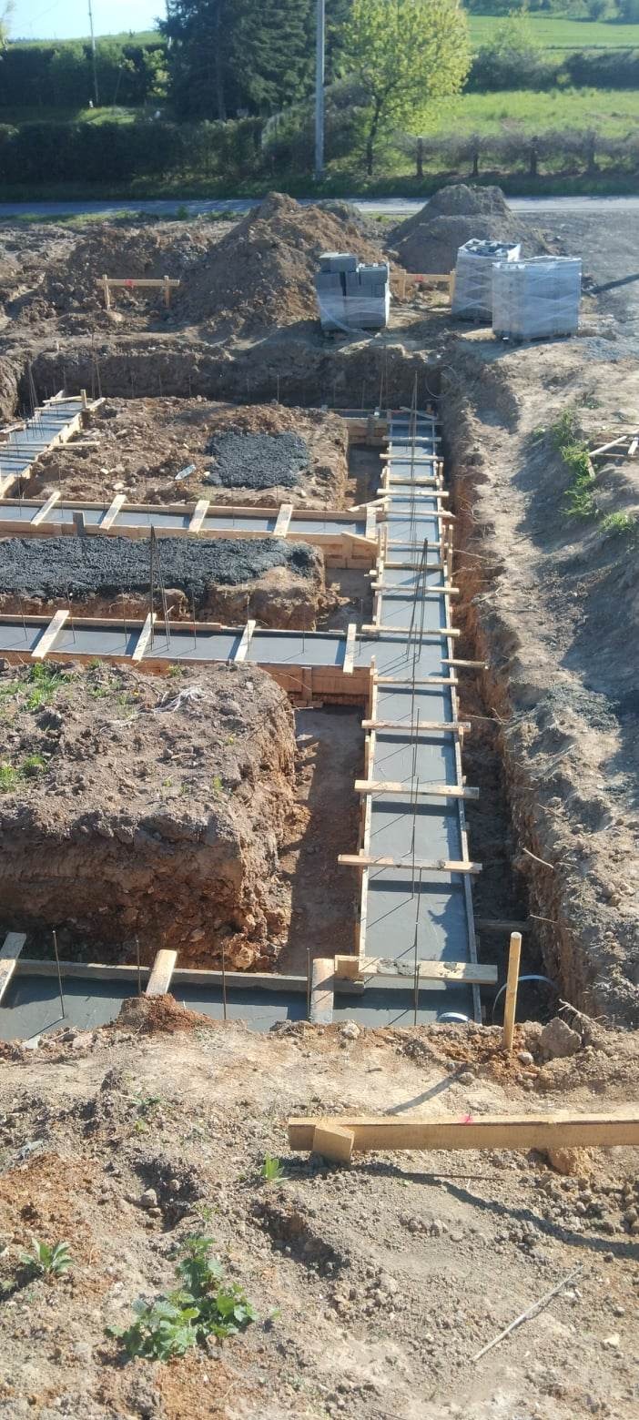 Wykop pod fundamenty z deskowaniem i zalanym betonem, widoczne zbrojenie, w tle ułożone bloczki fundamentowe.