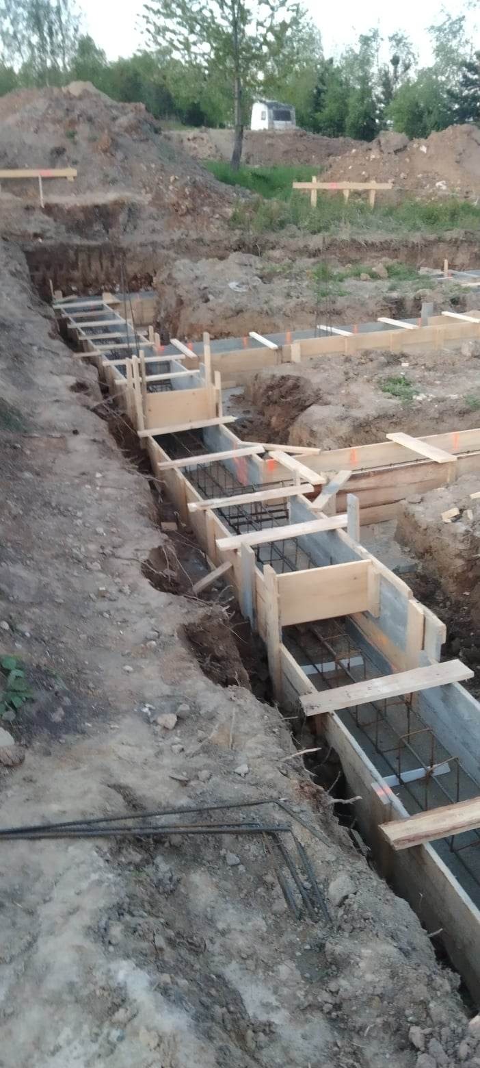 Wykop pod fundamenty z szalunkiem drewnianym i zbrojeniem stalowym, przygotowany do zalania betonem.