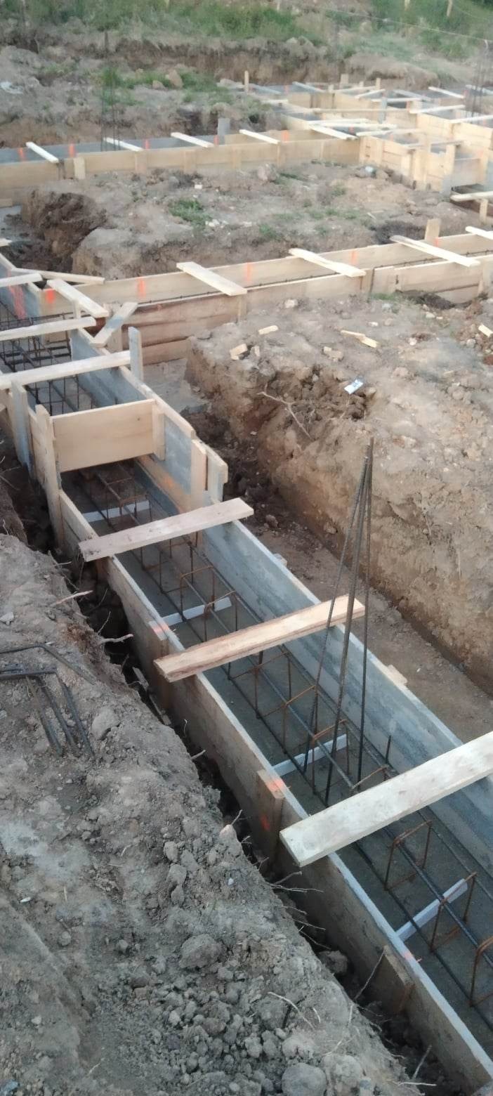 Wykop pod fundamenty z szalunkiem drewnianym i zbrojeniem stalowym, widoczne elementy konstrukcyjne w ziemi.