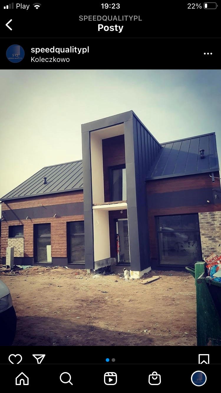 Nowoczesny dom w trakcie wykończenia elewacji, z elementami drewnianymi i grafitowymi, widoczne rusztowania i teren budowy.