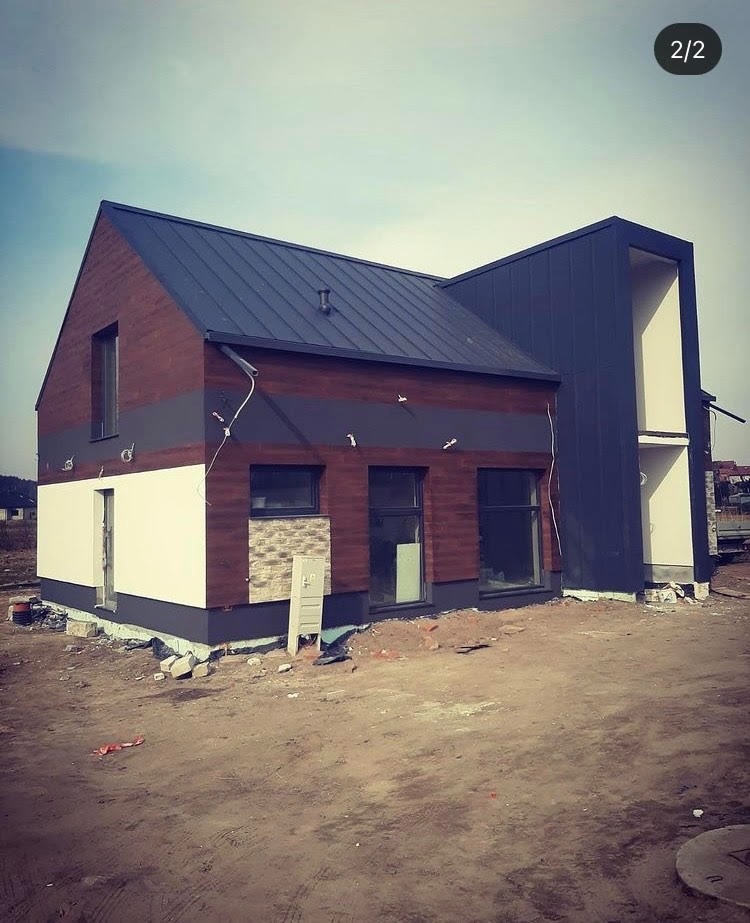 Nowoczesny dom w trakcie wykończenia elewacji z elementami drewna, tynku i kamienia dekoracyjnego, widoczne przygotowania do dalszych prac.