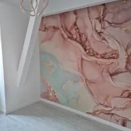 Pusty pokój z abstrakcyjną tapetą w odcieniach różu, złota i błękitu, nowoczesna lampa wisząca, białe ściany i panele podłogowe imitujące drewno.