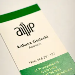 Wizytówka z logo i danymi kontaktowymi adwokata Łukasza Gieleckiego, z zielonymi akcentami na górze i dole, leżąca ukośnie na jasnym tle.