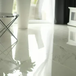 Błyszcząca, marmurowa podłoga w jasnym salonie z chromowanym stolikiem kawowym i białymi donicami w tle, odbijająca światło okna.