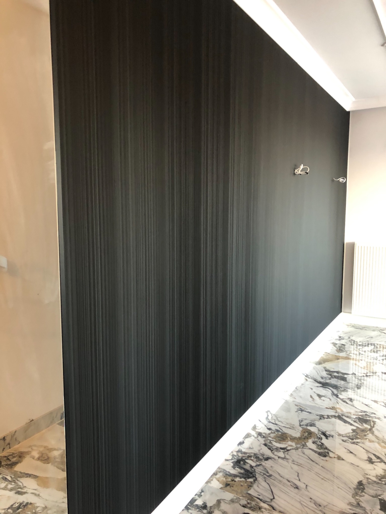 Nowoczesna, ciemna tapeta w pionowe prążki na ścianie w domu w Wagańcu, z widocznymi przygotowanymi punktami elektrycznymi i marmurową podłogą.
