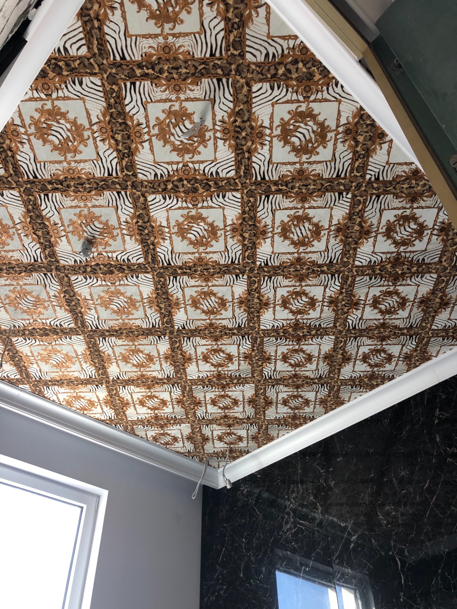 Dekoracyjny sufit kasetonowy z motywem zwierzęcym i ornamentami w kolorze złota, wykończony białym profilem przysufitowym, widok z dołu.