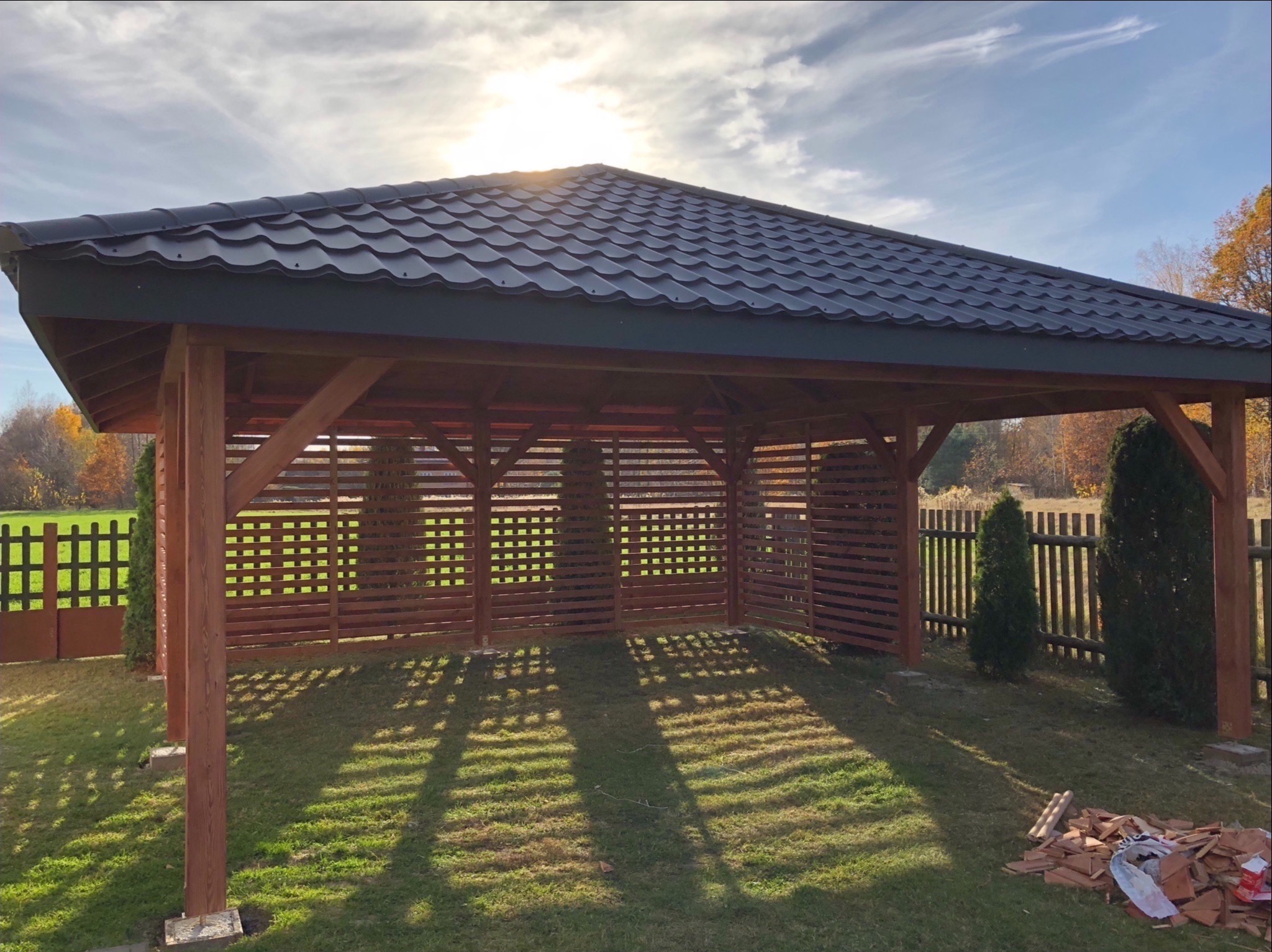 Zadaszona konstrukcja z drewnianą kratownicą w Sokołowie Małopolskim, z ciemnym dachem i rozproszonym światłem słonecznym, obok leżą dachówki.
