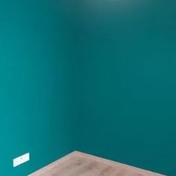 Pomalowany na turkusowo róg pokoju z jasnymi panelami podłogowymi i wiszącą białą lampą z abażurem