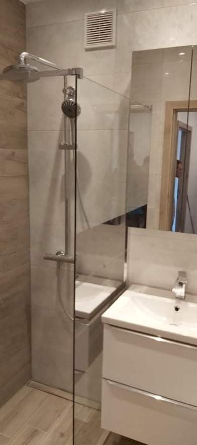 Nowoczesna łazienka z kabiną prysznicową typu walk-in z deszczownicą, umywalką nablatową na białej szafce i lustrem, wykończona płytkami w odcieniach beżu i szarości.
