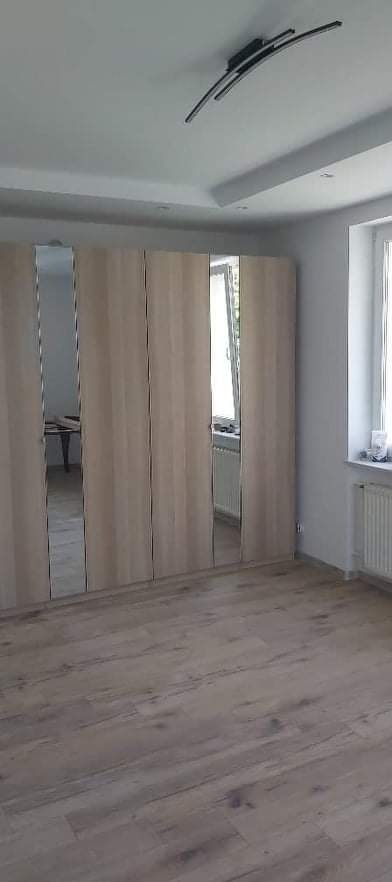 Jasny pokój z drewnianą podłogą i szafą z lustrami, nowoczesna lampa na suficie.