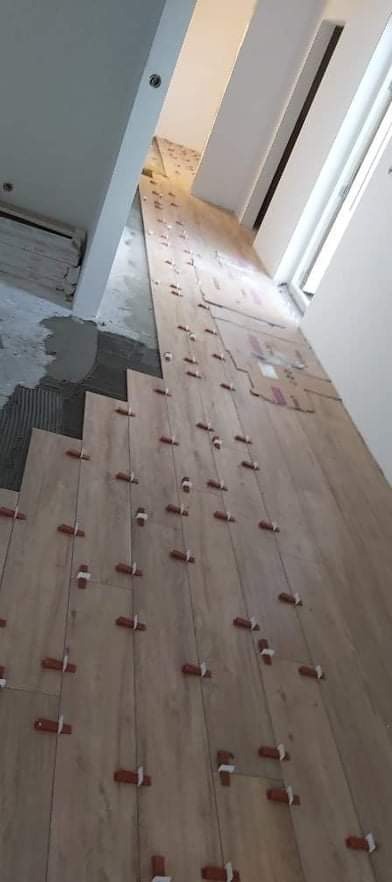 Układanie podłogi z płytek imitujących drewno, z użyciem krzyżyków dystansowych, widoczny fragment świeżo nałożonego kleju i przygotowane paczki płytek.