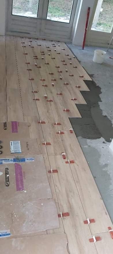 Układanie podłogi z paneli drewnopodobnych w trakcie remontu, widoczne krzyżyki dystansowe, poziomica oparta o ścianę i kartony zabezpieczające podłogę.