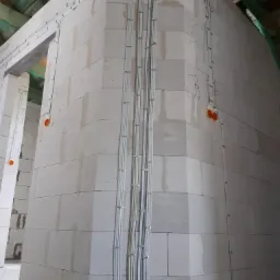 Wewnętrzna instalacja kabli elektrycznych w nowo budowanym domu z białych bloków, kable prowadzone po ścianach i pod sufitem, widoczne puszki elektryczne w kolorze pomarańczowym.