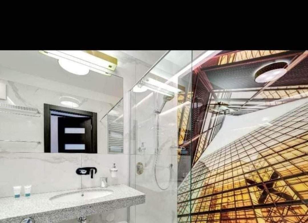 Nowoczesna łazienka z marmurowymi płytkami, szklaną kabiną prysznicową i umywalką z blatem z szarego granitu, odbicie budynku biurowego w szkle.