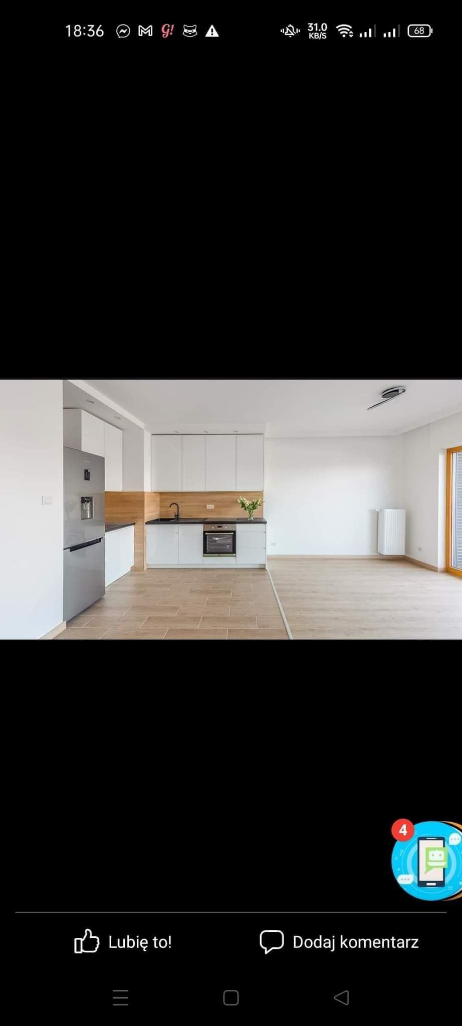 Nowoczesna kuchnia z białymi szafkami i drewnianym panelem nad blatem, widok na otwartą przestrzeń salonu z jasną podłogą i grzejnikiem.