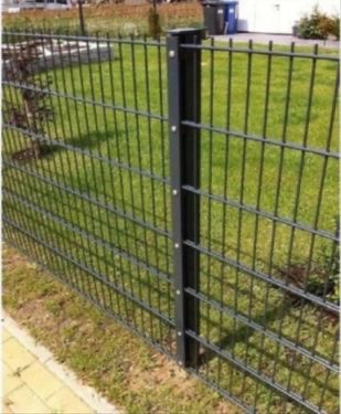 Szare, metalowe ogrodzenie panelowe z prostokątnymi oczkami, zamontowane na metalowych słupkach, widok z bliska na tle trawnika i zabudowań.