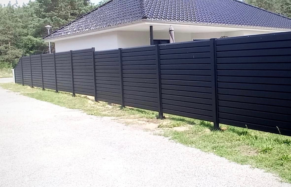 Nowoczesne, czarne ogrodzenie panelowe z poziomych desek kompozytowych, widok od strony drogi, dom z szarą dachówką w tle.