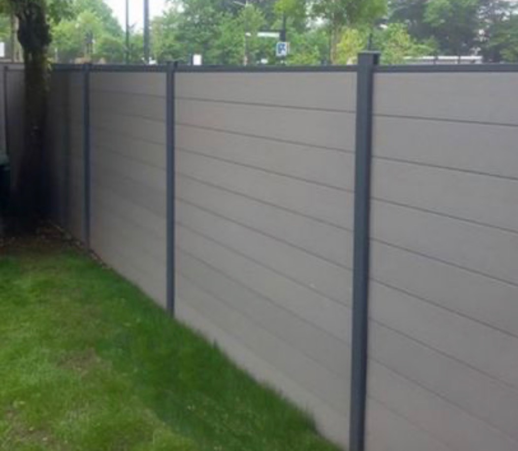 Długi, nowoczesny płot z poziomych, szarych paneli kompozytowych z ciemnoszarymi słupkami, widok z niskiej perspektywy na trawnik i drzewa w tle.