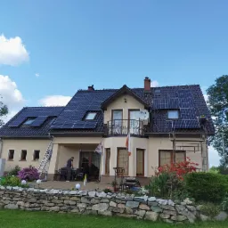 Instalacja paneli słonecznych na dachu domu jednorodzinnego w Kamiennej Górze; widoczni dwaj monterzy, drabina i rusztowanie.