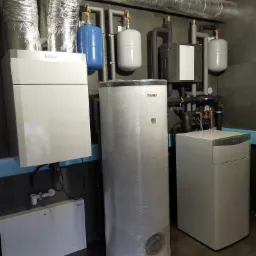 Kompleksowa kotłownia z rekuperacją, zbiornikiem i piecem Vaillant, zainstalowana w Kamiennej Górze, z widocznymi rurami wentylacyjnymi pod sufitem.